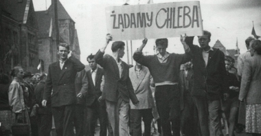 Pochód robotników. Trzech mężczyzn na przodzie trzyma transparent z napisem "Żądamy chleba". Po prawej stronie idzie Janusz Kulas.